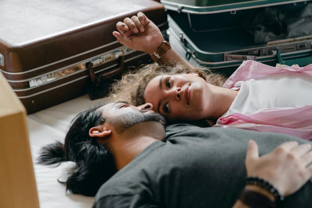 From above of young woman and ethnic man lying together near opened suitcase and resting during relocate into new contemporary apartment
